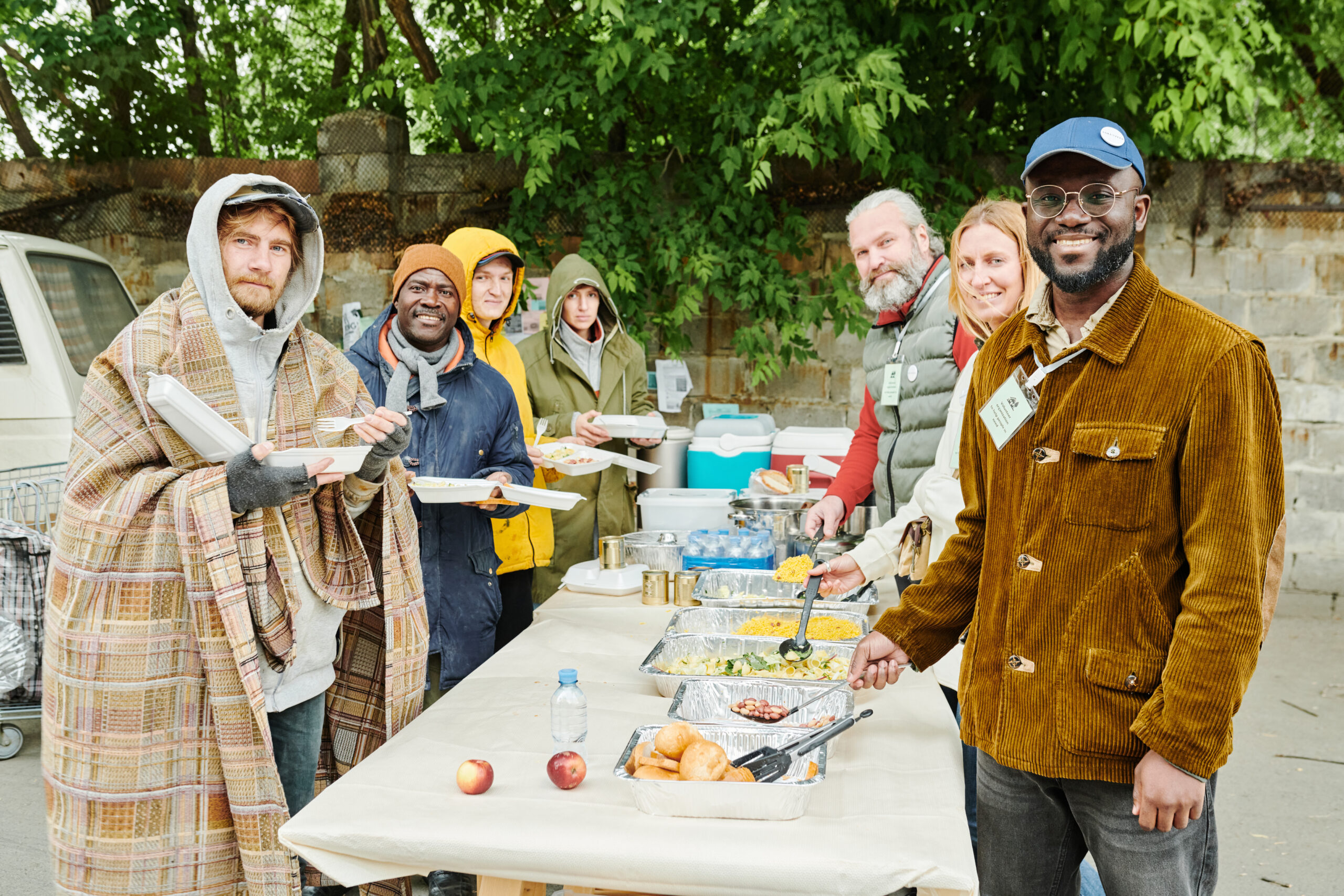 Portrait of group of volunteers and homeless people smiling at camera while arranging charity for beggars