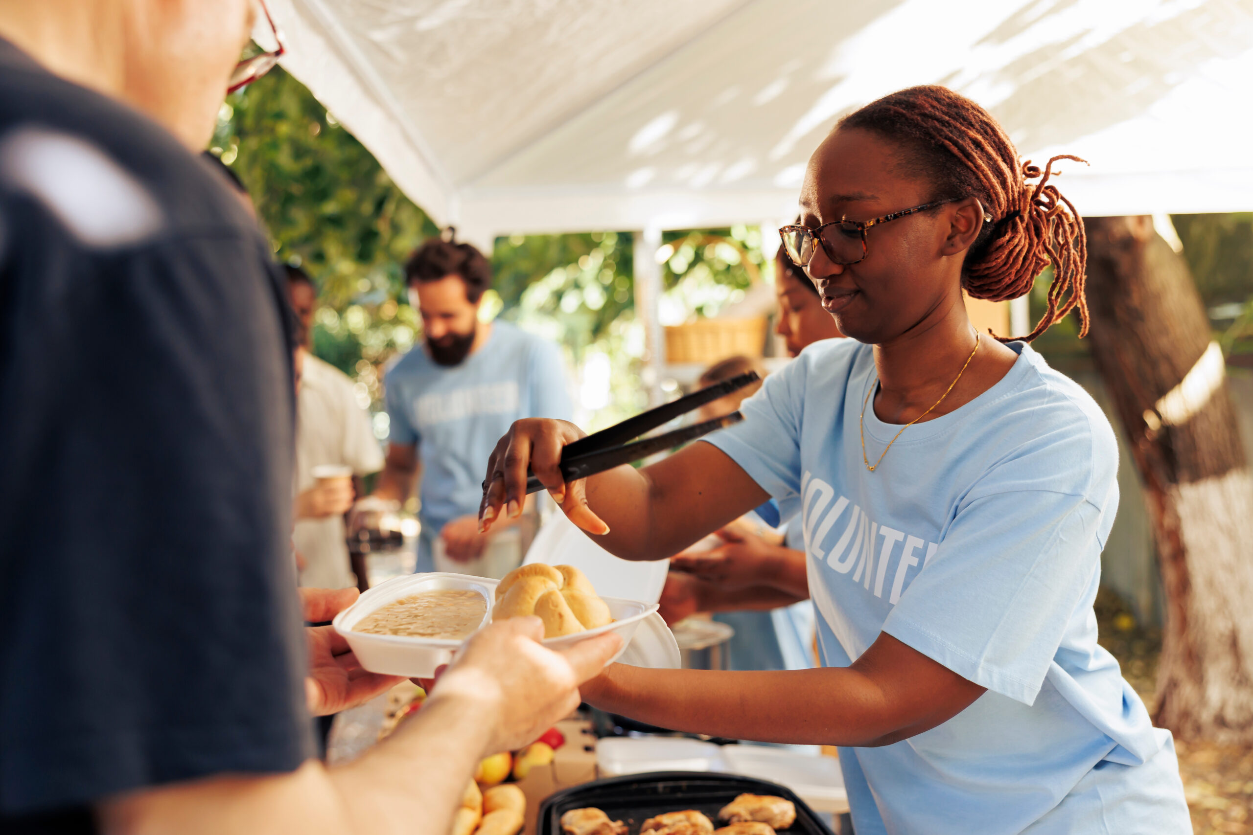 Detailed image of black woman at a food drive sharing free warm meals to poor caucasian homeless person. At local center group of volunteers feed and support the hungry and underprivileged.